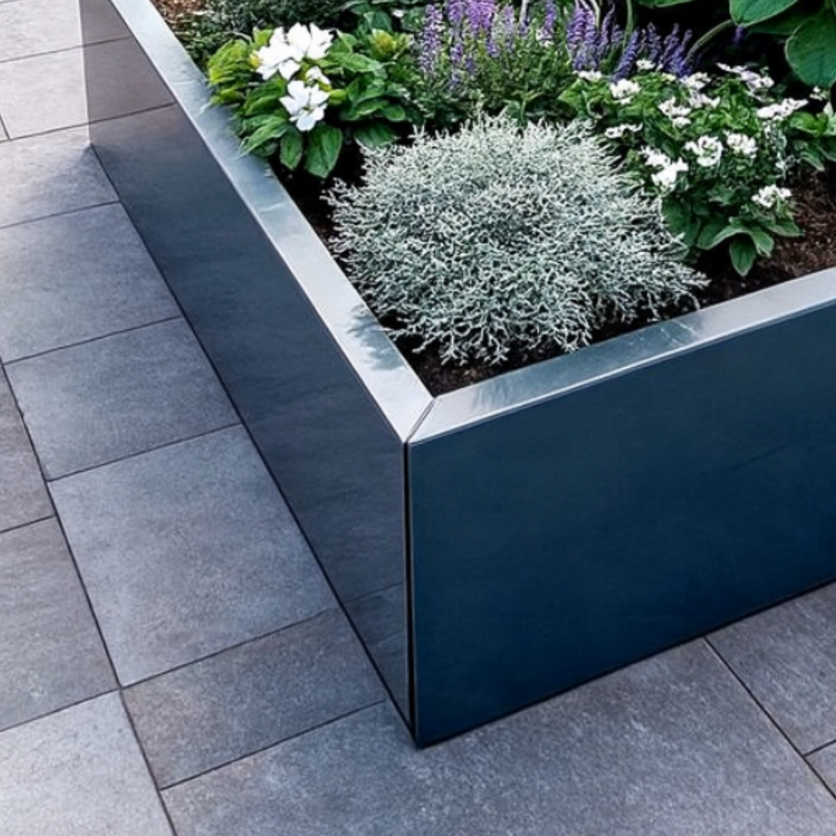 Detail van een luxe donkergrijze metalen plantenbak met strakke afwerking, gevuld met zilverstruikje, witte bloeiers en paarse salvia op een modern terras.