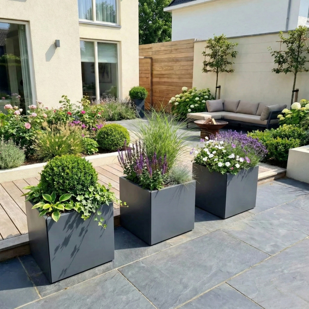 Hoge vierkante plantenbak met een groene bolvormige plant op een strak betegeld terras bij een moderne woning.