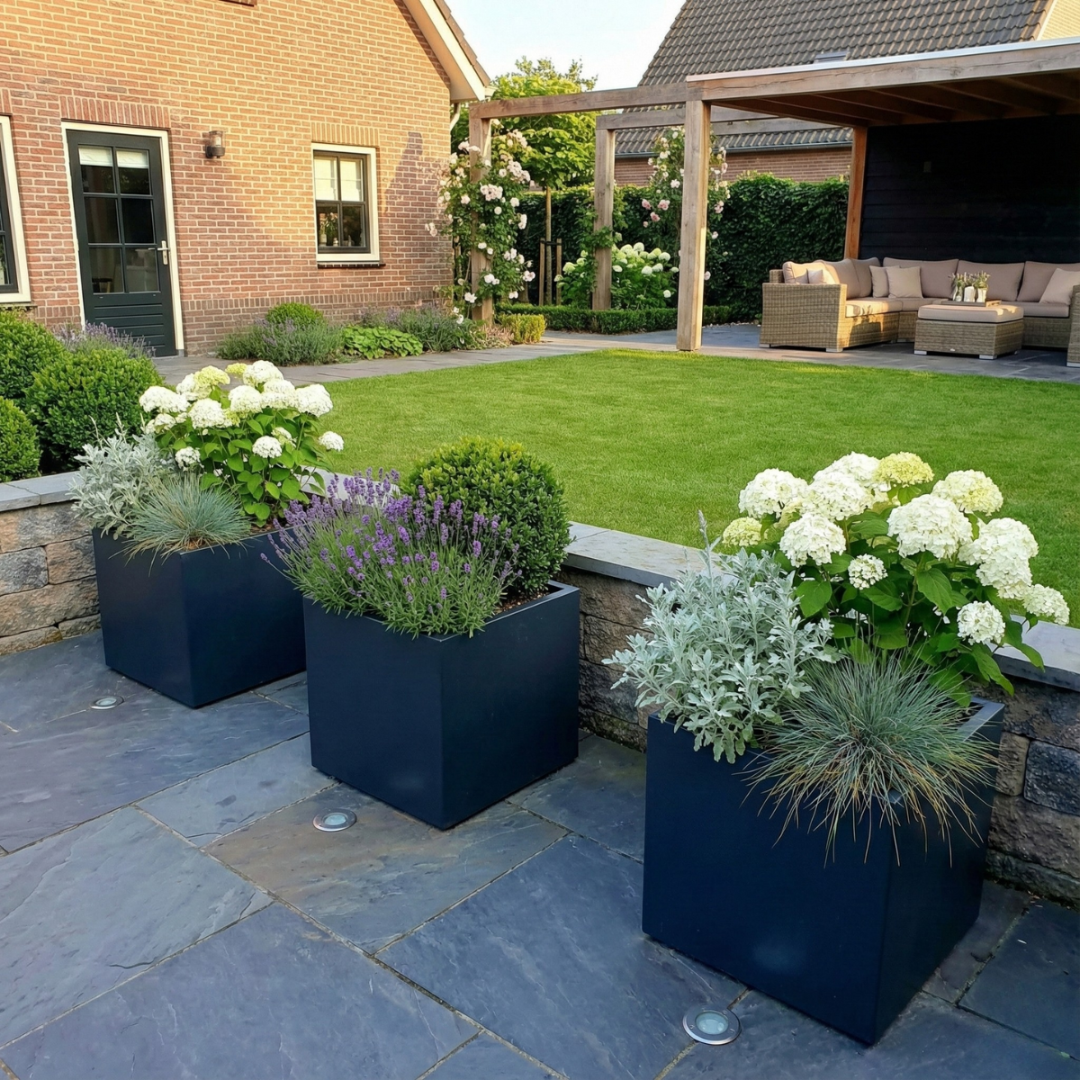 Drie donkergrijze vierkante plantenbakken sfeervol opgesteld op een terras met blauwe tegels, gevuld met een frisse mix van witte hortensia's, paarse lavendel en grijsbladig zilverstruikje.