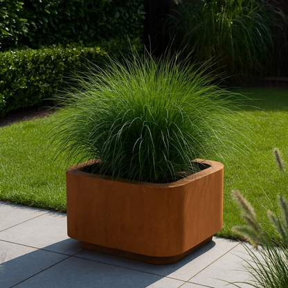 Een cortenstaal plantenbak gevuld met groen siergras in een tuin.