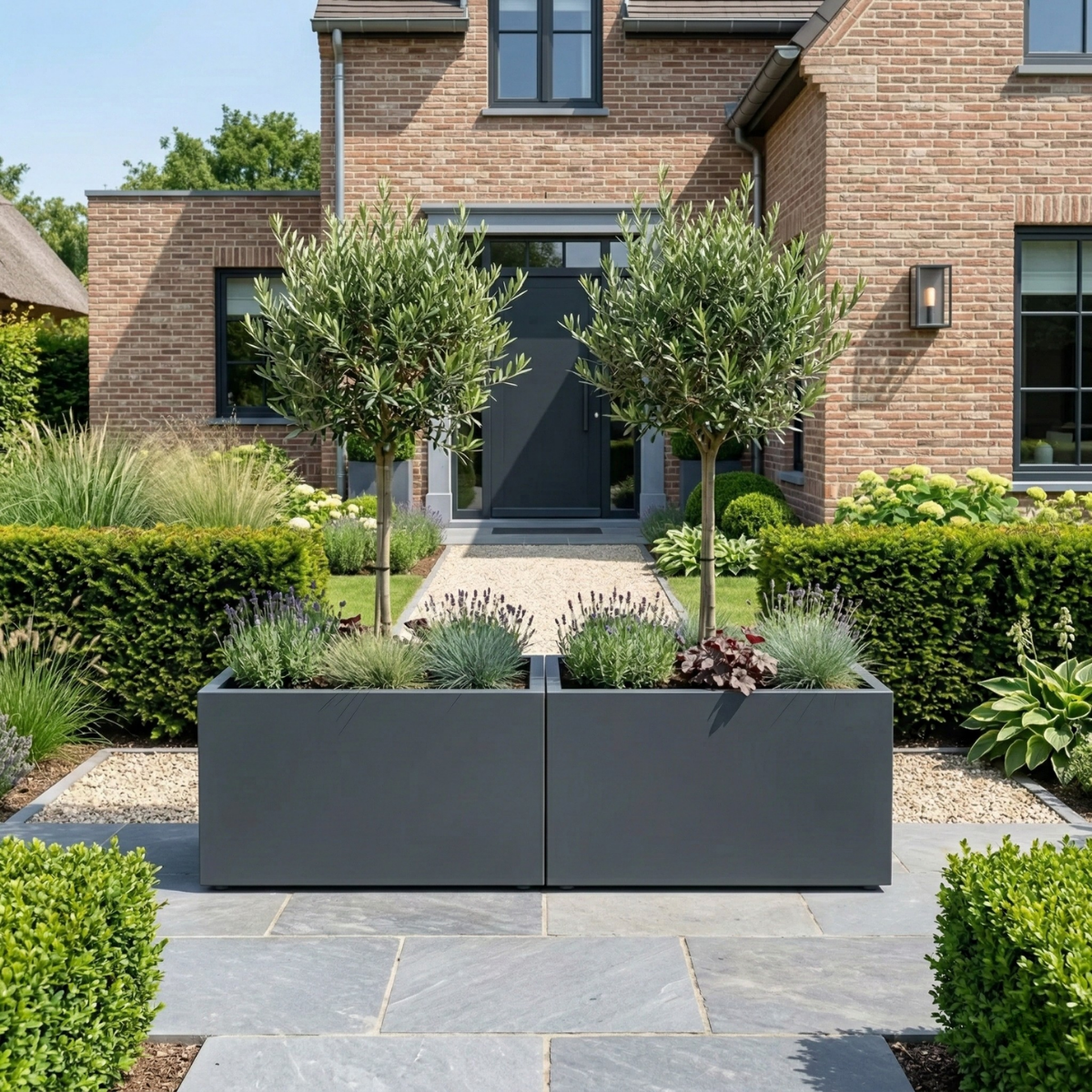 Grote rechthoekige donkergrijze plantenbakken gevuld met lavendel en siergrassen op een betegeld terras in een sfeervolle voortuin.