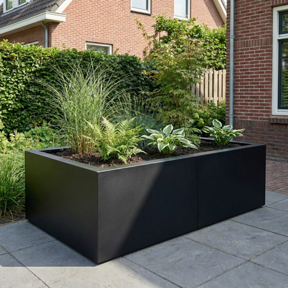 Zwarte plantenbak gevuld met siergrassen en varens op een betegeld terras in een tuin.